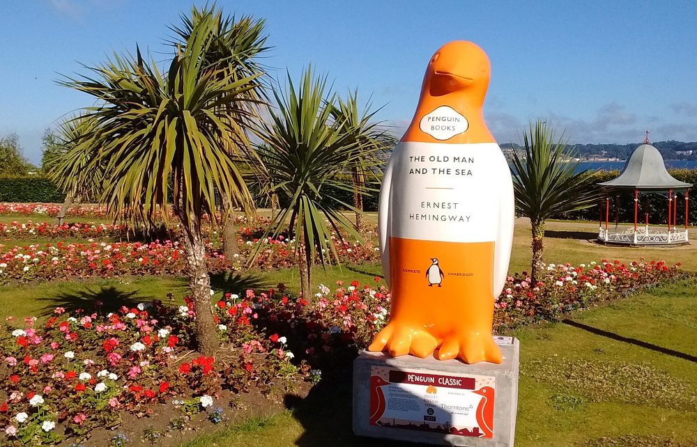 Orange and white penguin statue surrounded by flowers and palm trees at Maggie's Penguin Parade, Dundee, Scotland