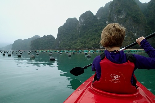 Girl kayaking around pearl farm buoys in Halong Bay, Vietnam